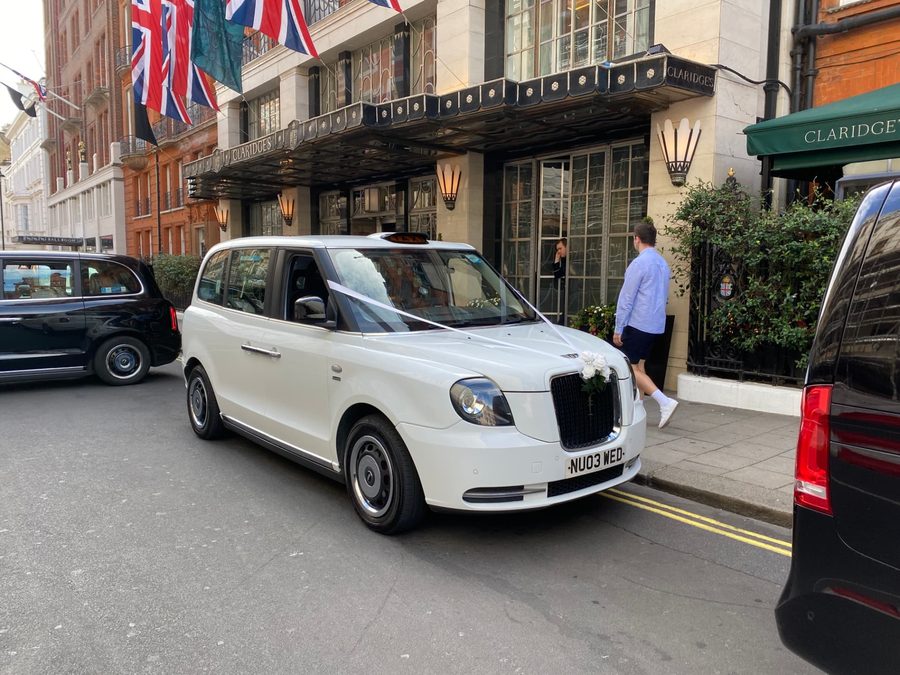 White electric TXE wedding taxi with ribbons and flowers outside Claridge's in Mayfair