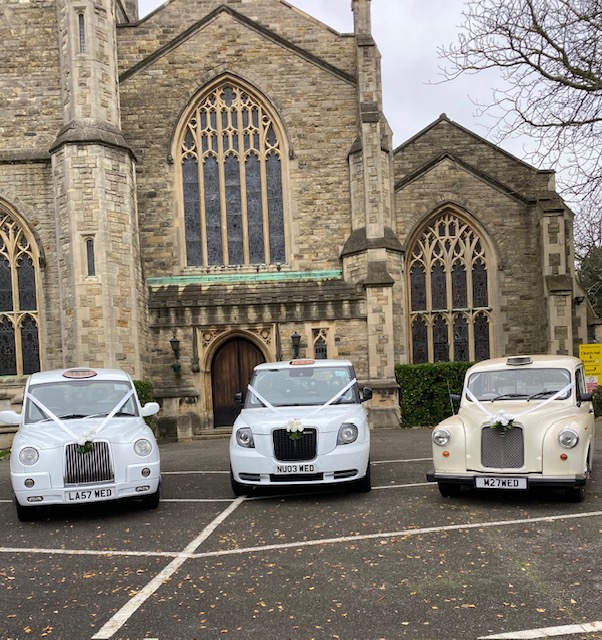 Three white wedding taxis outside a church