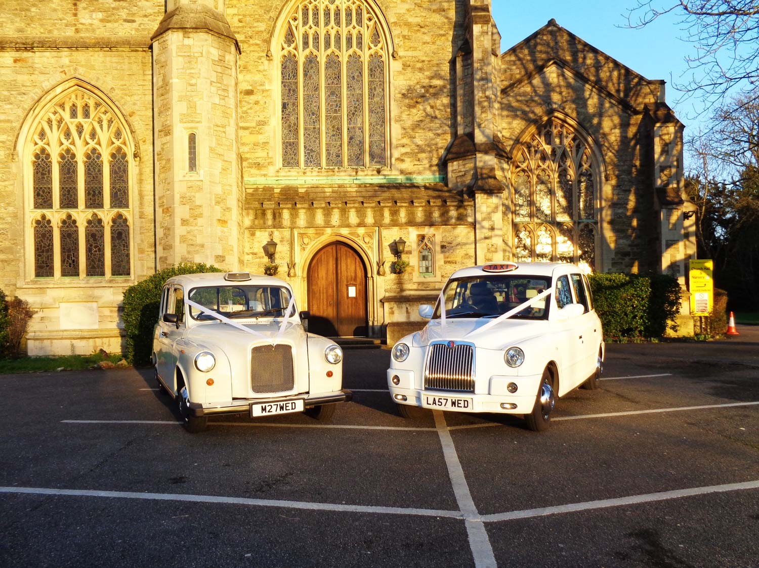 Two white wedding taxis outside a church