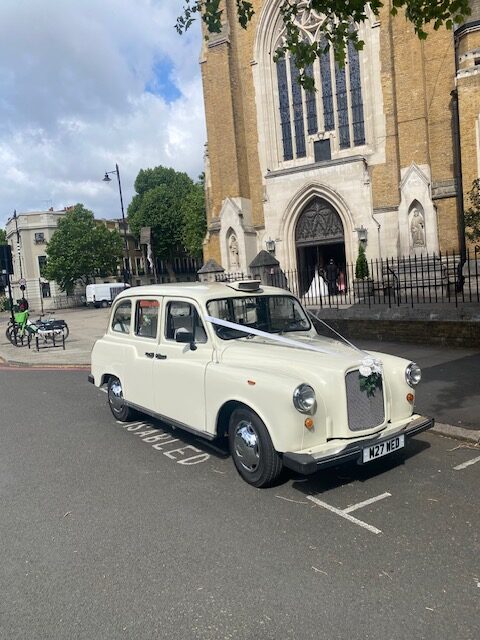 Classic Fairway wedding taxi with roses and ribbons waiting outside a church