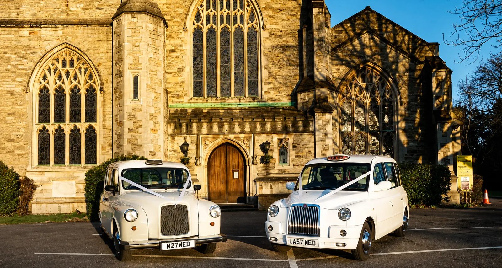 Classic Fairway and electric TXE wedding taxis with ivory ribbons outside a church