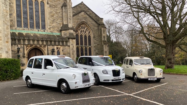 Three white wedding taxis outside a church